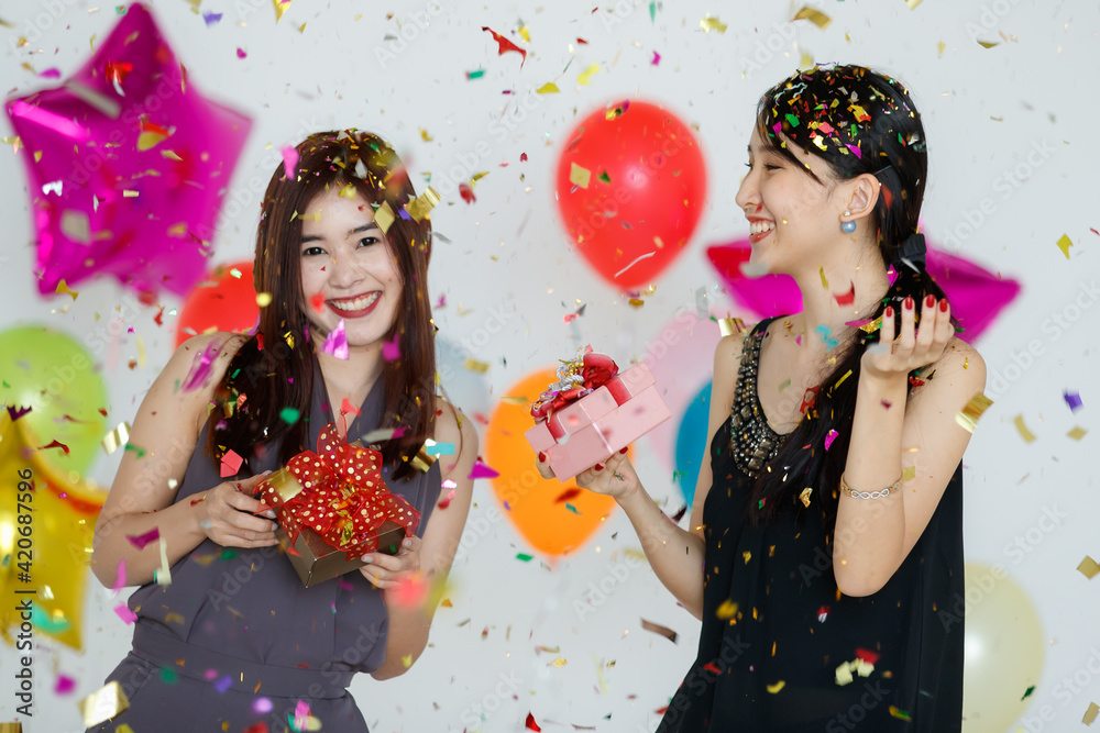 Delighted Asian girlfriends standing under confetti Delighted Asian girlfriends standing under confetti