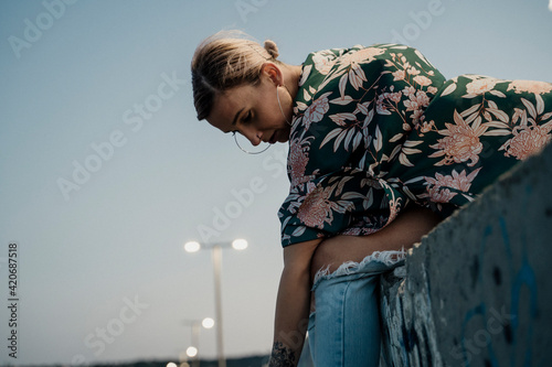 Young stylish woman sitting on top of wall with graffity with pensive face looking down photo
