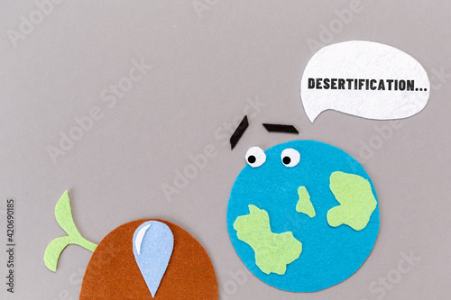Desertification. Cutted out of felt the planet with emoticon and dry soil with a dead plant sprout. Gray background. Flat lay. Concept of envronment protection photo