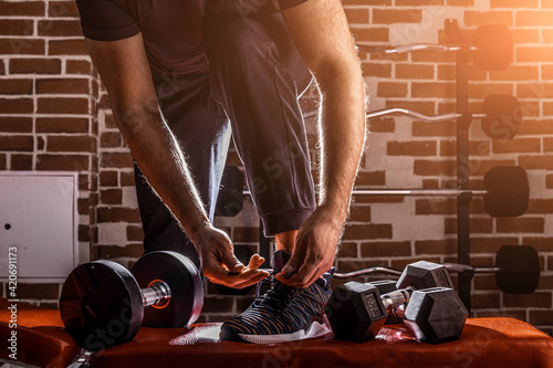 Fitness motivation and muscle training concept. Man in sneakers tying shoelaces in sunlight. Athlete starting exercise with dubbell weight. photo