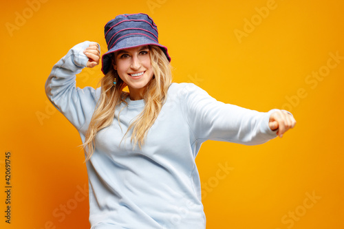 Stylish girl in panama hat dancing against yellow background