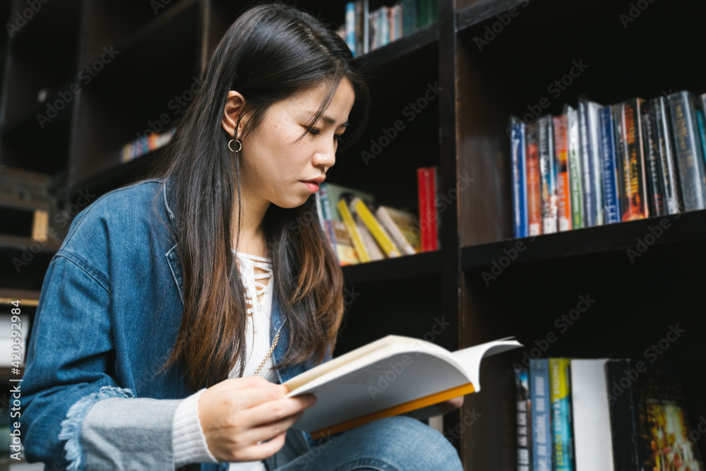 © zheng long/Stocksy - Young woman reading in the library