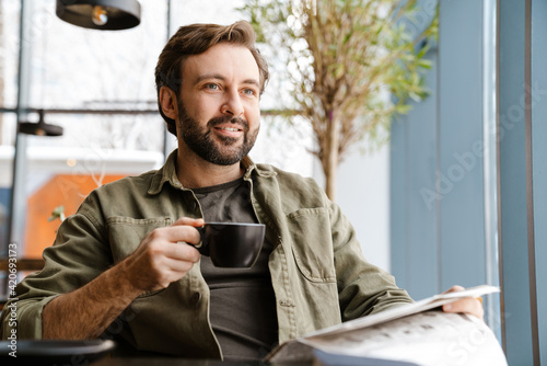 Unshaven focused man drinking coffee while reading newspaper in cafe
