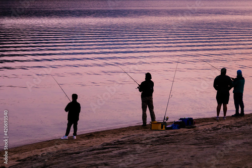 several fishermen with fishing rods on the shore of a lake catch fish, silhouette view, before Kovid 19 photo