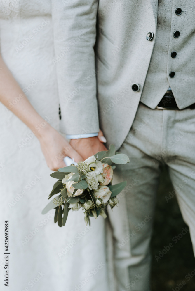 Bride and groom holding a small bouquet with roses, peonies and eucalyptus Bride and groom holding a small bouquet with roses, peonies and eucalyptus