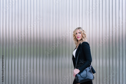 portrait of a business woman walking with her handbag on a gray metal background. Elegant business woman walking in the city. Business concept 
