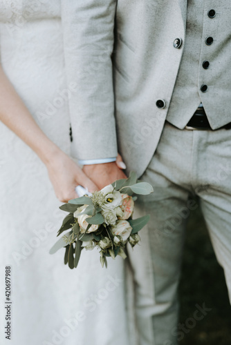 Bride and groom holding a small bouquet with roses, peonies and eucalyptus photo