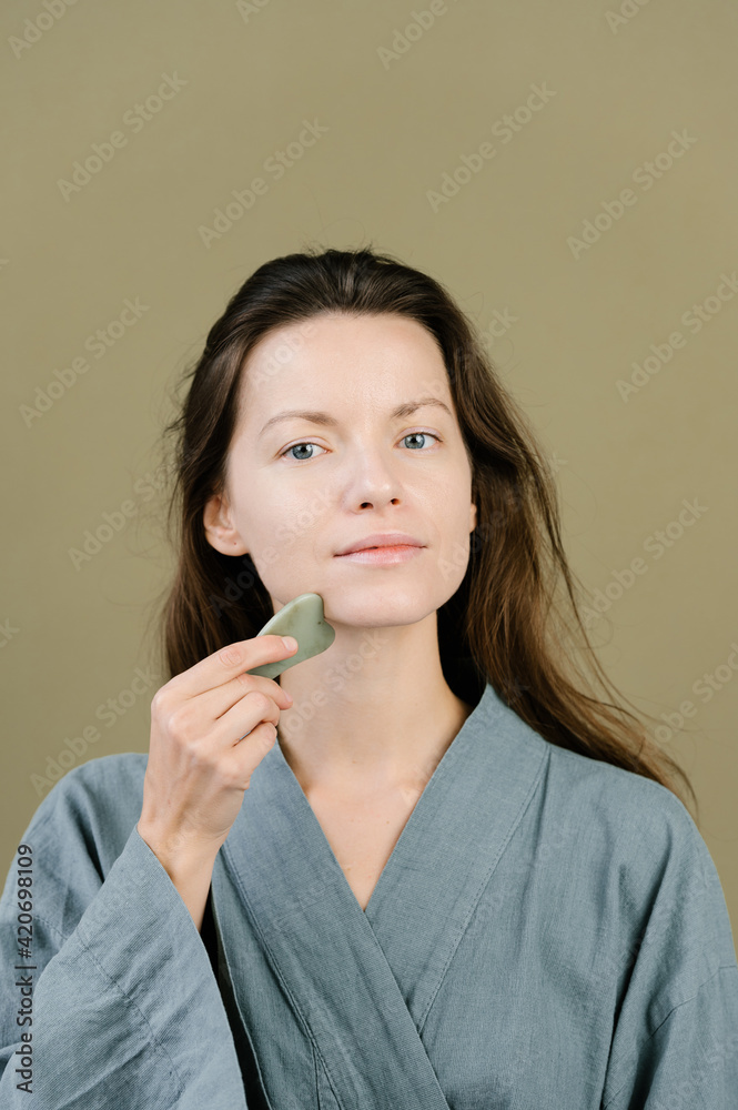 Calm woman massaging face with gua sha scraper in studio Calm woman massaging face with gua sha scraper in studio