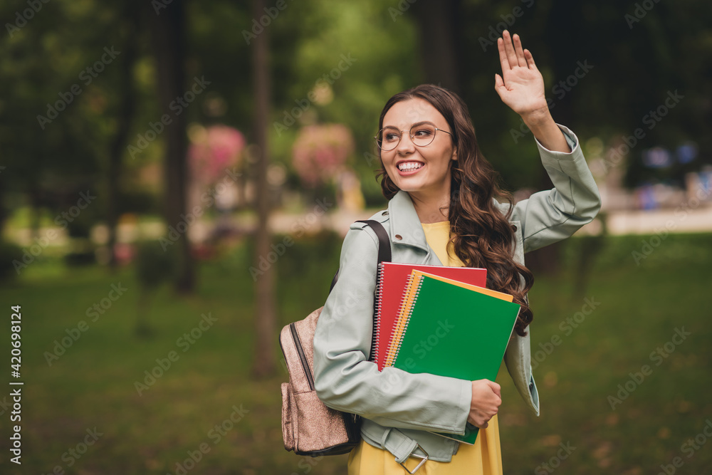 Fototapeta premium Portrait of adorable friendly person carry rucksack copybook look far away arm palm wave have good mood outdoors