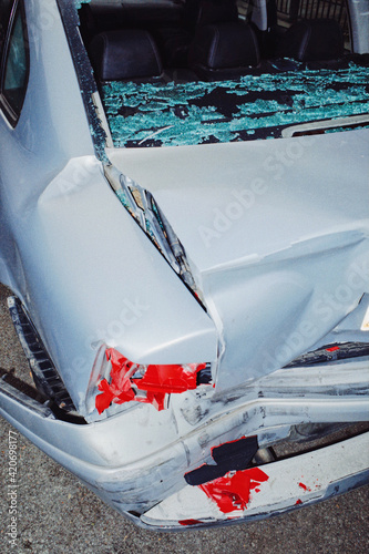 Gray car parked on the street with back window shattered and a bad dent in the bumper photo