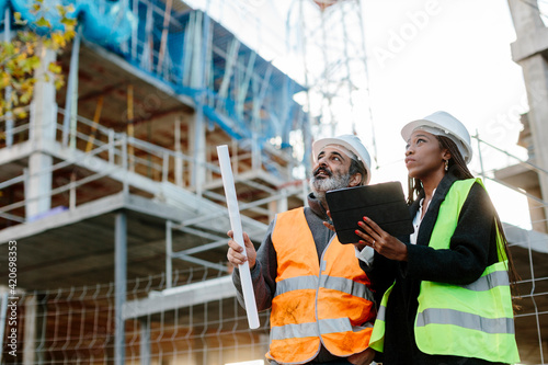 Woman engineer supervising construction of building with construction worker checking her tablet device photo