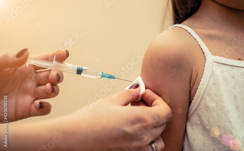 Little girl in the doctor s office is vaccinated. Syringe with vaccine against covid-19 coronavirus  flu  infectious diseases. Injection after clinical trials for human  child. Medicine concept.