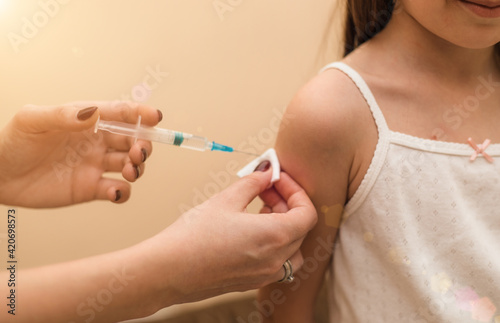 Little girl in the doctor s office is vaccinated. Syringe with vaccine against covid-19 coronavirus  flu  infectious diseases. Injection after clinical trials for human  child. Medicine concept.