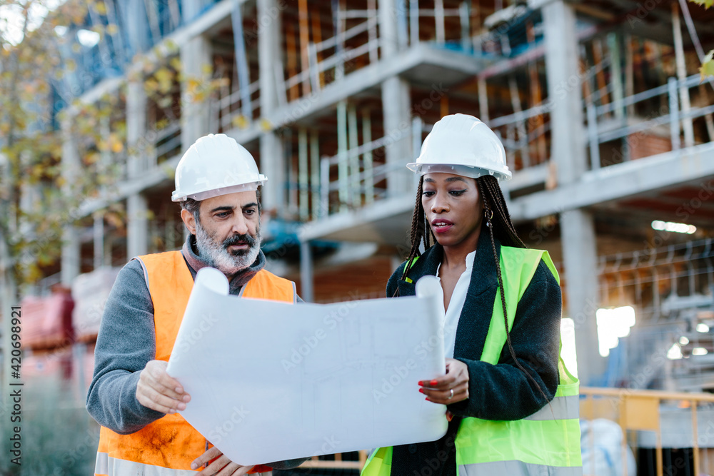 © Jimena Roquero/Stocksy - Woman engineer and construction foreman checking blueprints in front of a building in construction. © Jimena Roquero/Stocksy - Woman engineer and construction foreman checking blueprints in front of a building in construction.