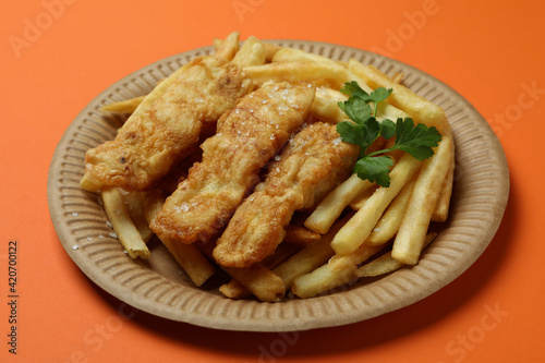 Plate with fried fish and chips on orange background