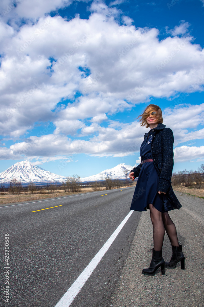 a beautiful blonde girl Millennial in a dress stands by the road against the background of a volcano in Kamchatka, went on a trip after quarantine covid-19 and self-isolation