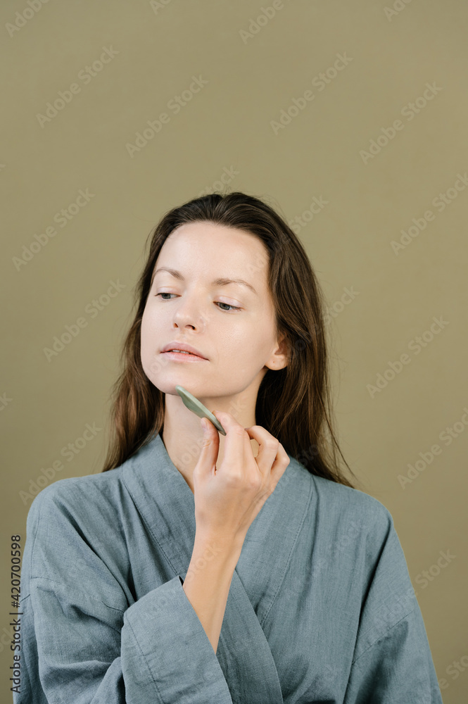 Tranquil woman applying gua sha massager on face Tranquil woman applying gua sha massager on face