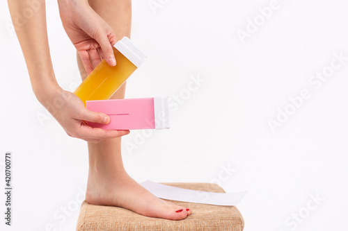 Close-up of the hand of a young woman using a modern rechargeable roll-on waxer for removing hair from her legs at home. Two type of warm wax, natural and rosa. Different liposoluble wax cartridges photo