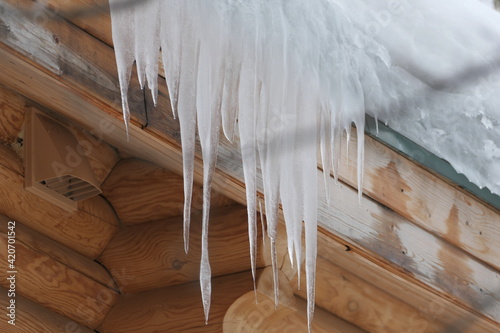 Large icicles hang from the roof of a log house