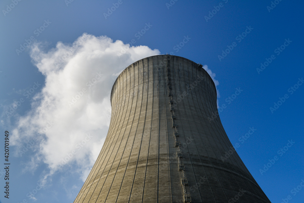Contre-plongée d'une tour d'une centrale nucléaire d'où sort de la vapeur d'eau en fumée blanche sur fond de ciel bleu