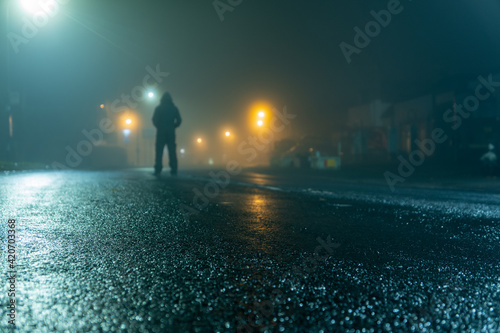 A low angle of a hooded figure standing in a street at night photo