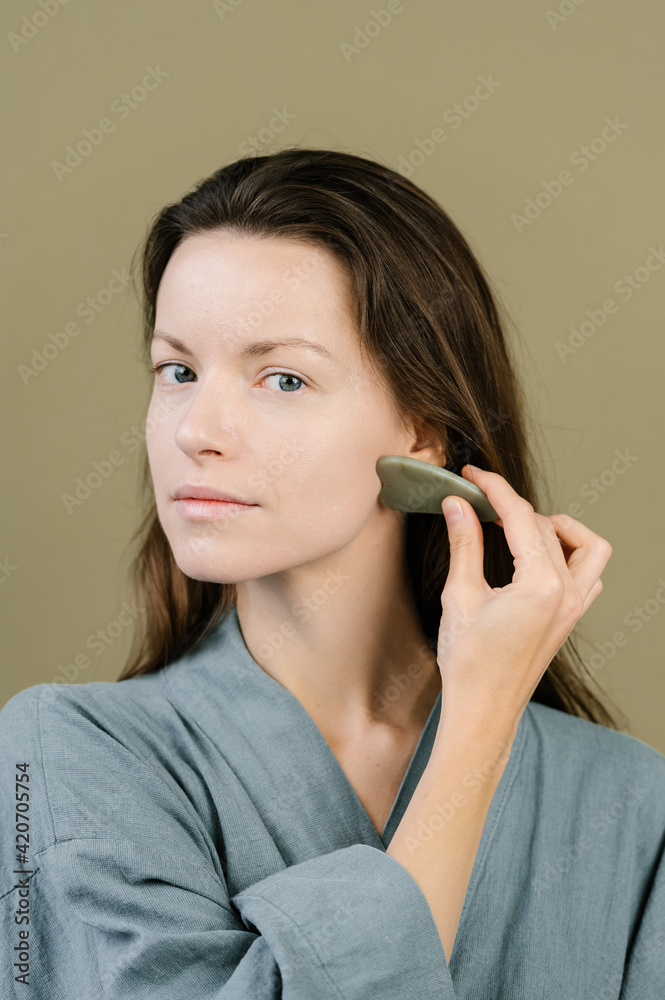 Calm woman massaging face with gua sha scraper in studio Calm woman massaging face with gua sha scraper in studio