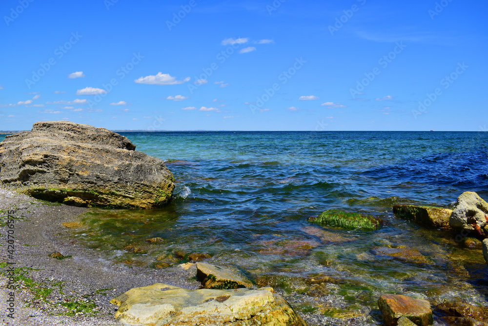 A picturesque seascape overlooking the blue sea, rocks and stones on a bright sunny day. The waves break against the rocks. the stone lies on the beach. coastline, leisure concept, tourism, vacation