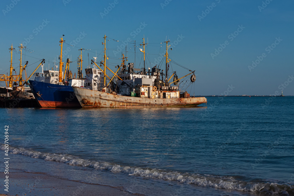 Old ships at the pier on the sea with an empty beach with clear blue water and sky. Seaport on the shore with cranes and boats. Wallpaper for desktop, poster, marine travel photo for post card design.