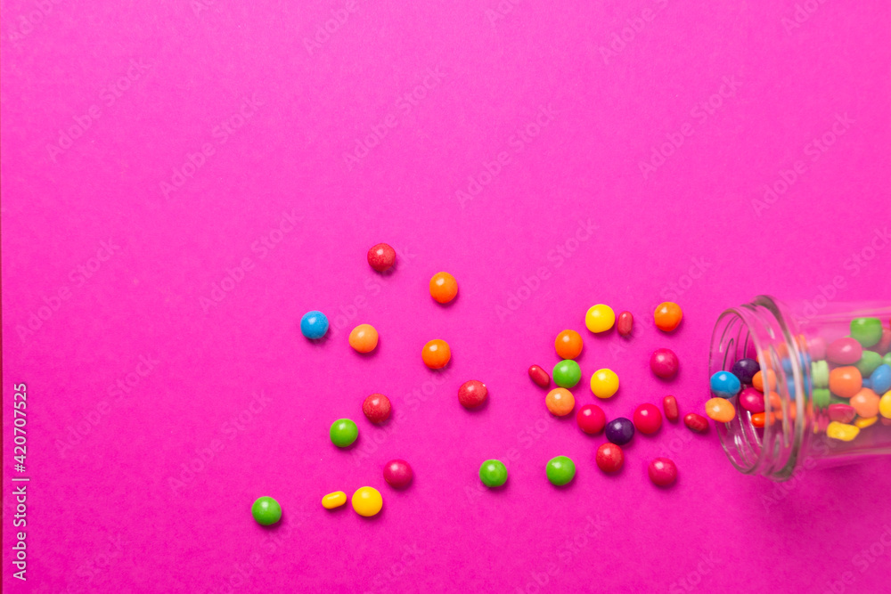 colorful candies poured from a glass jar on a colored background