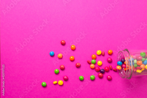colorful candies poured from a glass jar on a colored background