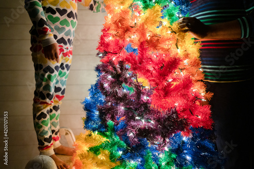 Faceless image of child and adult by rainbow Christmas tree