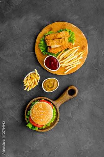 Burger served with french fries and fried chicken on wooden board. Top view