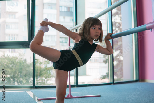 Beautiful girl gymnast in a black leotard doing stretching exercises. Sports club for girls photo