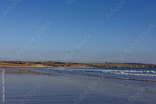 The exposed wet sand of the gently shelving beach at Lunan Bay as the Tide recedes  and lines of waves come in from the North Sea.