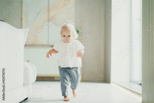 A cheerful mood. The child plays running around at home alone. Children and home. Portrait of a cute little girl with blonde blue eyes. The family spends time at home on the couch.