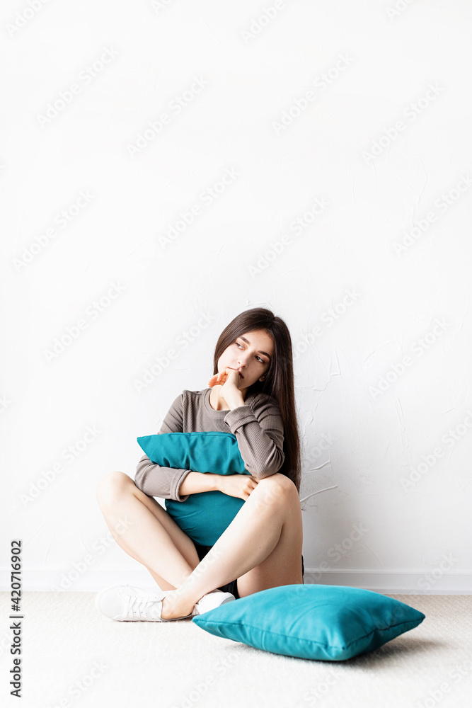 Beautiful young woman in casual clothes sitting on the floor with pillows