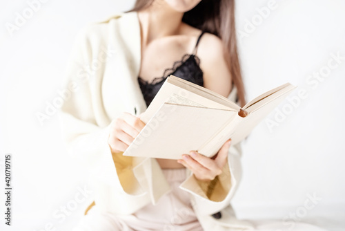 Beautiful smiling woman in comfortable home clothes reading a book sitting on the floor