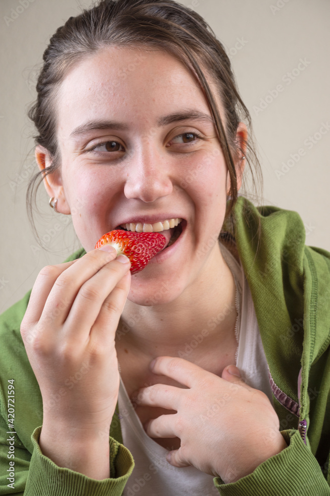 Close-up of smiling young woman, wearing sportswear, eating a strawberry that she is holding in her hand, vertical Close-up of smiling young woman, wearing sportswear, eating a strawberry that she is holding in her hand, vertical