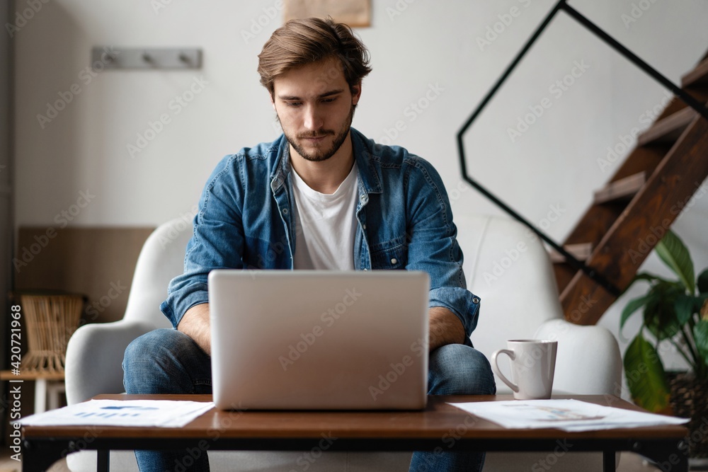 Entrepreneur working with a laptop and holding a document in a little office or home Entrepreneur working with a laptop and holding a document in a little office or home