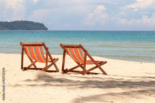 Sunbeds  deckchairs on the beach in front of tropical island.