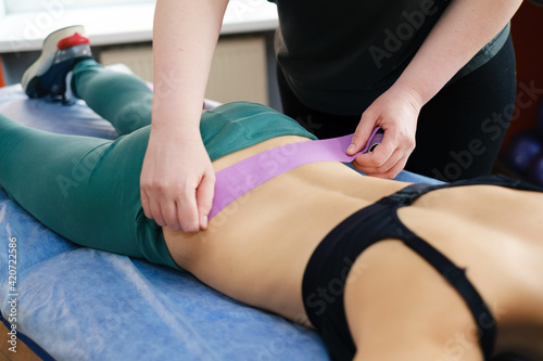 The physiotherapist massages the injured lower back of the athlete lying on the massage table with a kinesio tape. Masseur's hands holding the kinesio tape