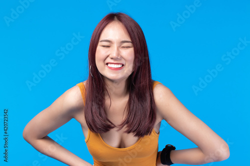 Fashion of a beautiful young asian woman in a pretty yellow vest White shorts. Girl posing smiling on blue background. fashion beauty and style.