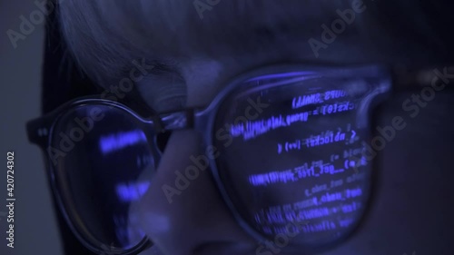 Close up of Programmer hacker working on computer. Code is reflected on his eye glasses. Guy committing cyber crime. Data thief, internet fraud, darknet and cyber security