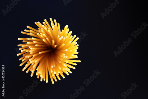 Raw dry spaghetti italian pasta yellow long line it looks like fireworks or flowers bloom on black background with copy space. Concept italian food background.