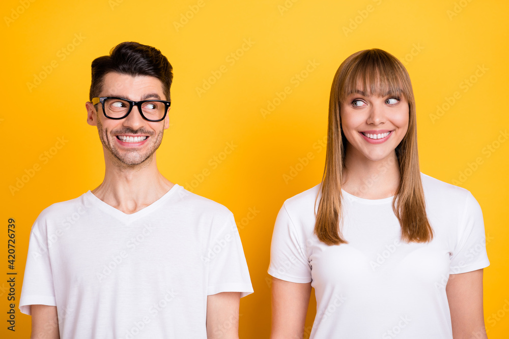 Photo of funny sweet young couple wear white t-shirt spectacles looking each other isolated yellow color background Photo of funny sweet young couple wear white t-shirt spectacles looking each other isolated yellow color background