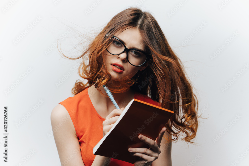 woman in an orange sundress on a light background with a notebook and a pen in her hand a student of education woman in an orange sundress on a light background with a notebook and a pen in her hand a student of education