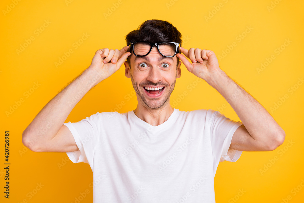 Photo of cute shocked young guy dressed white t-shirt arms glasses smiling isolated yellow color background Photo of cute shocked young guy dressed white t-shirt arms glasses smiling isolated yellow color background