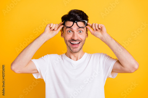 Photo of cute shocked young guy dressed white t-shirt arms glasses smiling isolated yellow color background