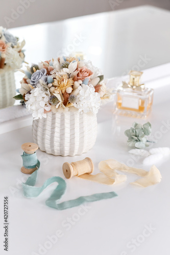 Bouquet with roses, hydrangea and spikelets in blue and beige colors. Stabilized flowers in a white ceramic vase at home on the dressing table. Interior decor.	