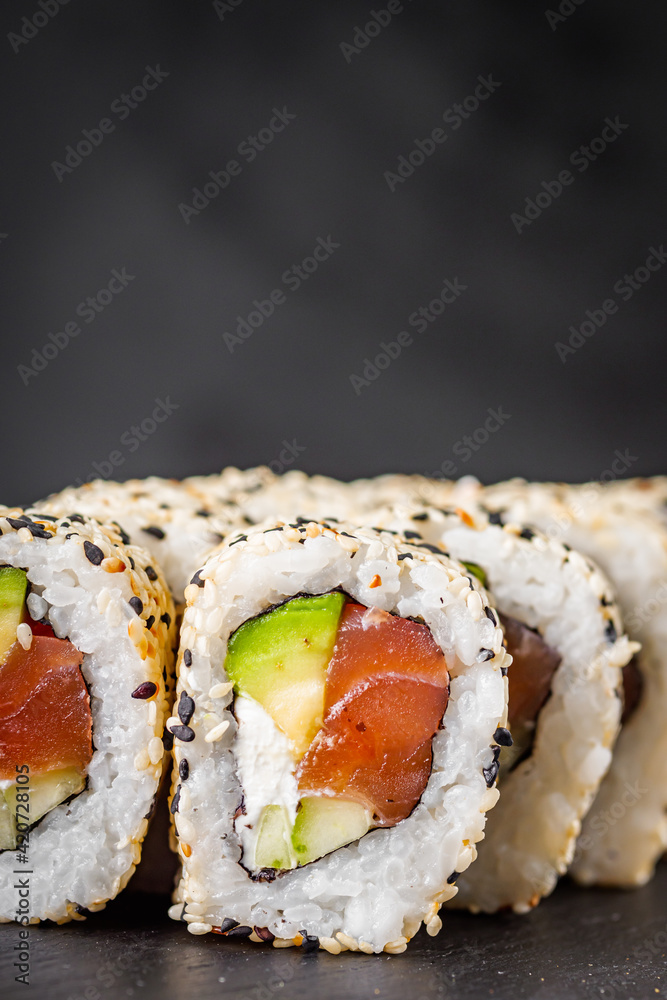 appetizing california sushi roll with cheese avocado cucumber and salmon in sesame seeds on a black stone plate appetizing california sushi roll with cheese avocado cucumber and salmon in sesame seeds on a black stone plate